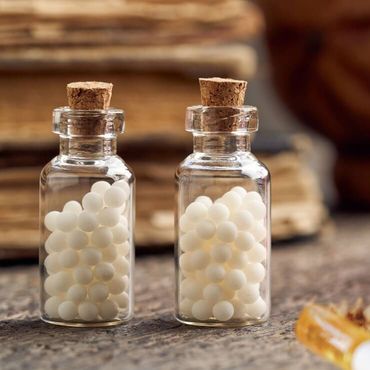 Glasflaskor med vita homeopatiska kulor placerad på ett naturligt underlag.