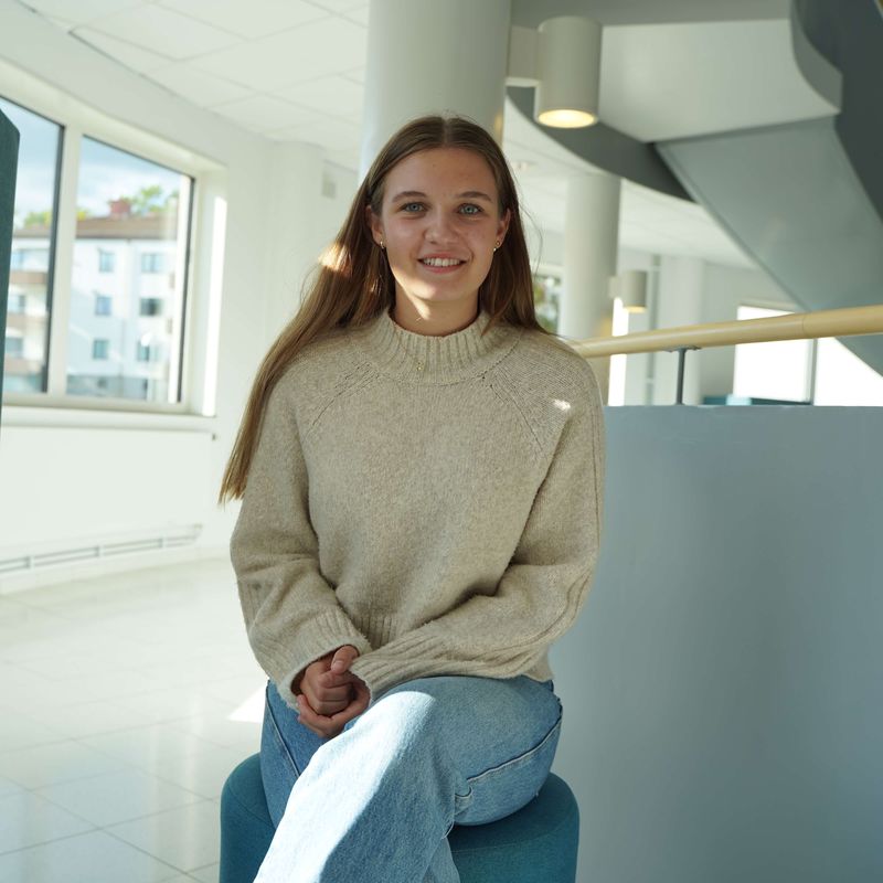 Felicia ler mot kameran, sitter på pall i Rotundan