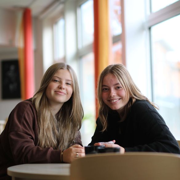 Två elever som ler mot kameran vid ett bord i matsalen