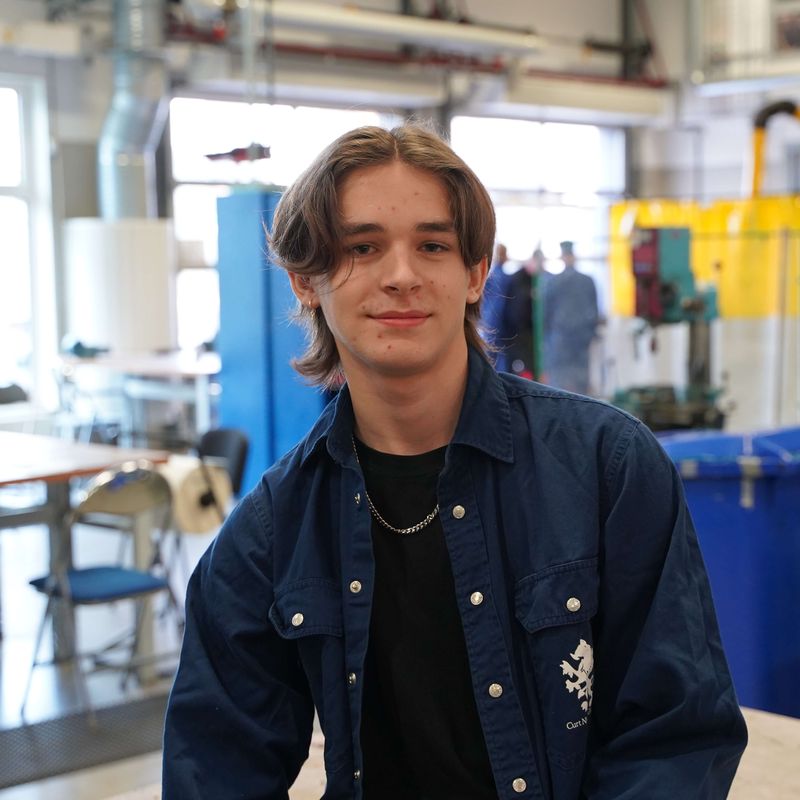 Ludvig ler mot kameran, sitter i verkstaden på CNG