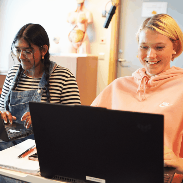 Två elever jobbar vid sina datorer och ler i vårdsalen på CNG