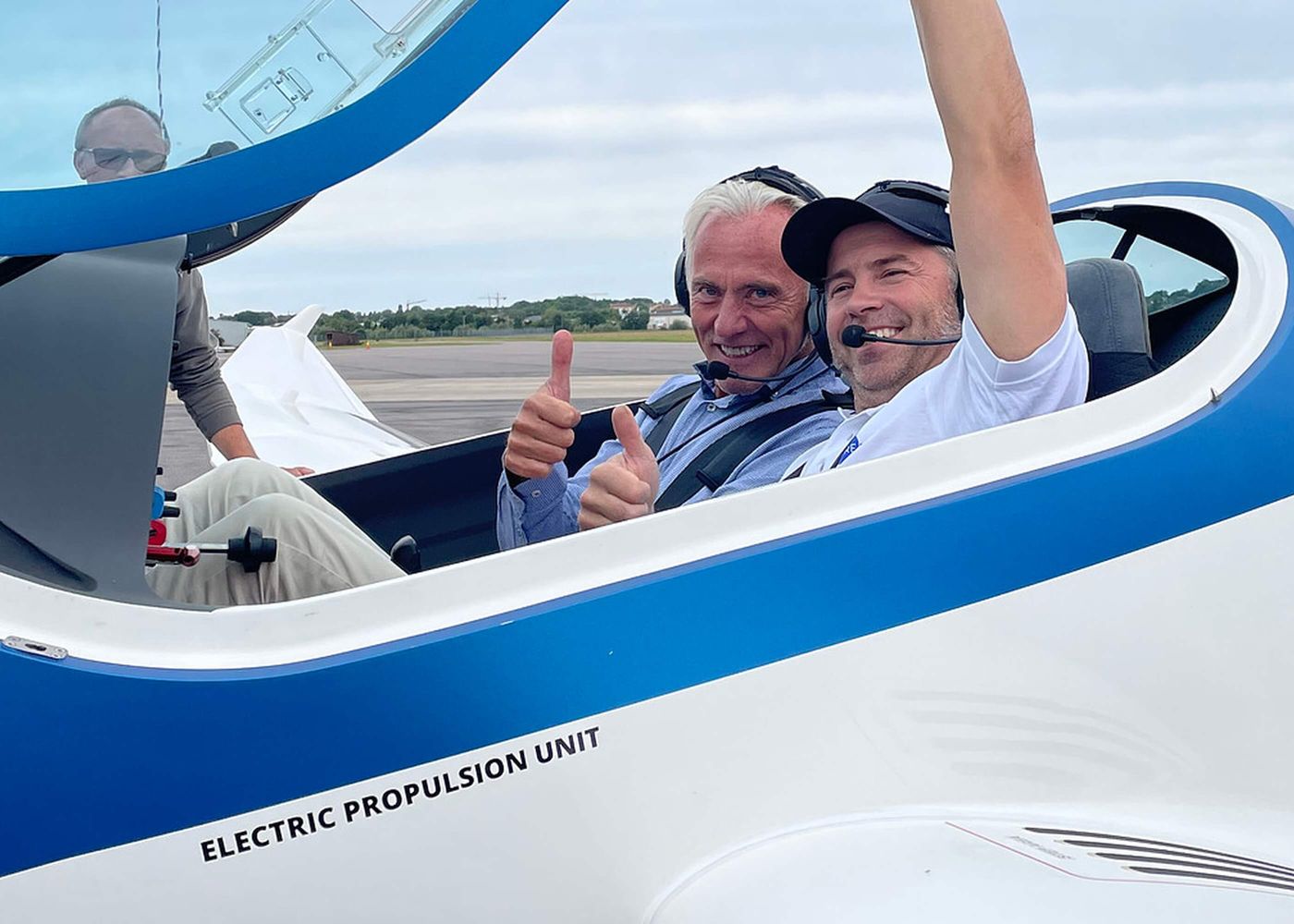 Två personer i cockpit på ett eldrivet småflygplan visar tummen upp och ler mot kameran.