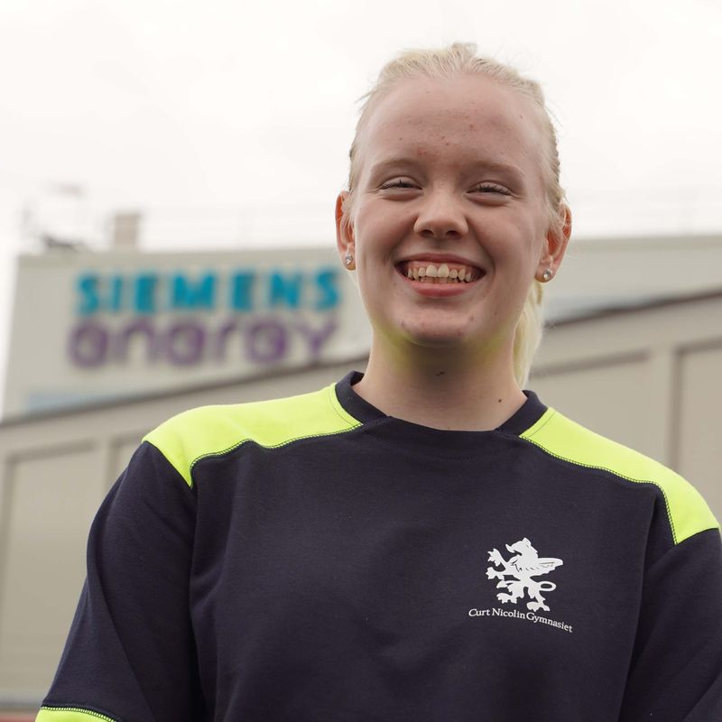 Freja ler mot kameran, Siemens Energys logga i bakgrunden