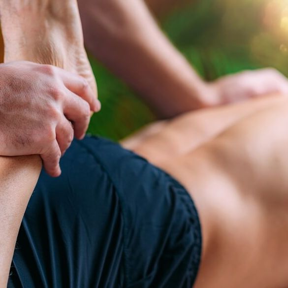 Massageterapeut stretchar ben och håller en hand på kundens skuldra