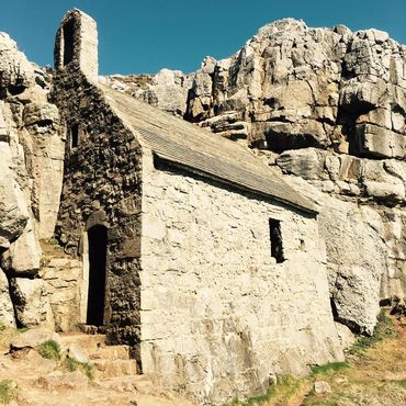 St Govan's Chapel is a 13th-century,, lime-washed stone structure built into a limestone cliff fissure on the Pembrokeshire Coast, Wales, marking a 6th-century hermitage site. It is associated with the Irish monk Govan—who allegedly hid there from pirates—and features a 6th-century holy well, ancient altar, and 52 steps. 
