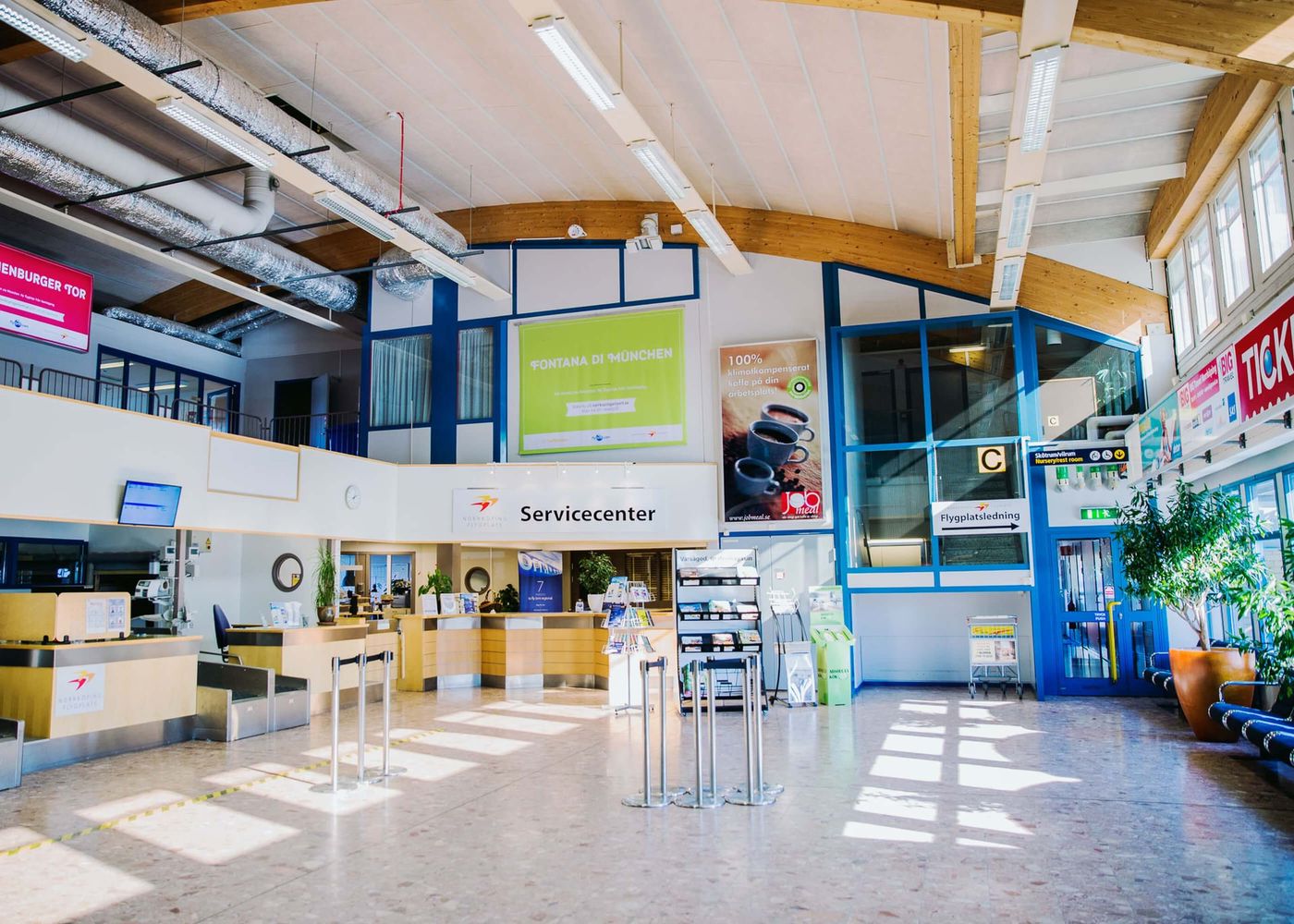 Ljust och modernt servicecenter inne på en flygplats med informationsdiskar, broschyrställ, skyltar och stora fönster som släpper in dagsljus.
