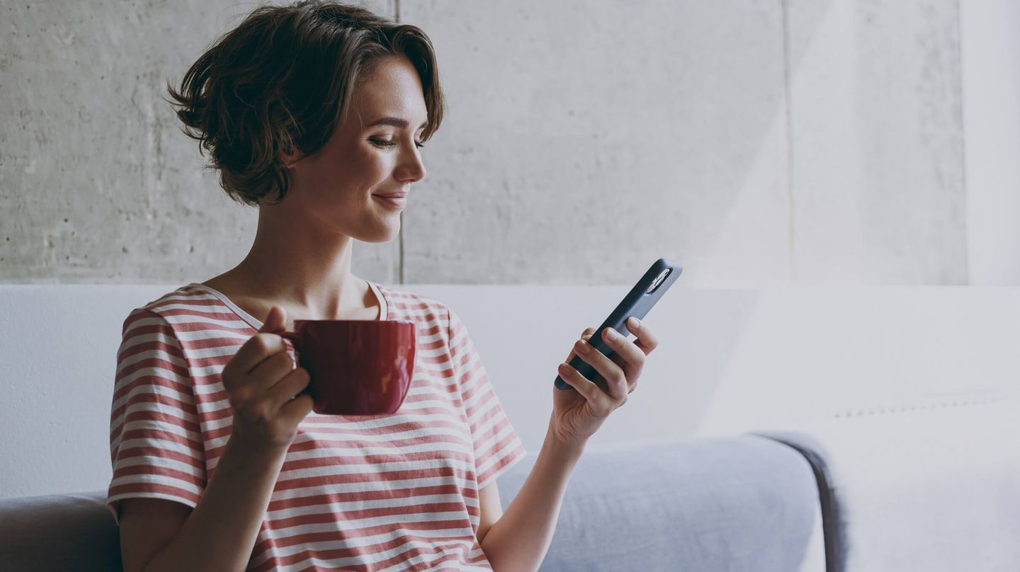 Woman with a tea cup in one hand and a mobile phone in the other