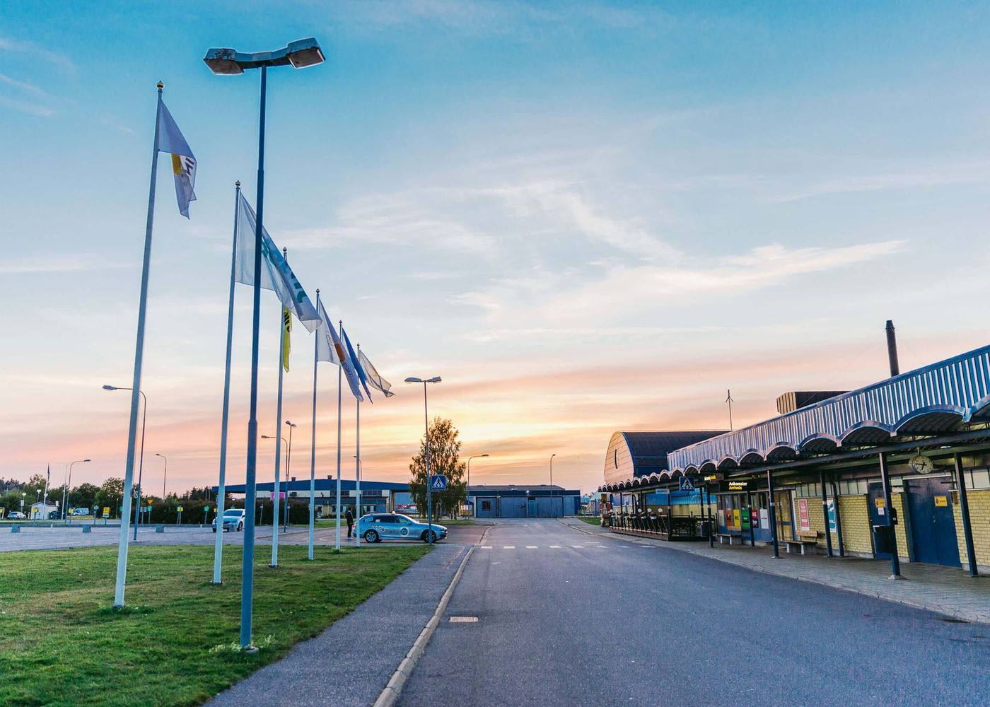 Flygplatsens entréområde med flaggstänger och upplyst himmel vid solnedgång