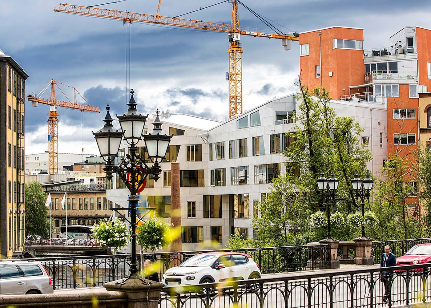 Stadsvy med moderna byggnader, byggkranar och klassisk gatubelysning i förgrunden.
